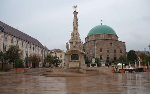 Pécs-Széchenyi tér-előtérben a Szentháromság szobor, háttérben a Gázi Kaszim pasa dzsámija. Fotó: Kőszály